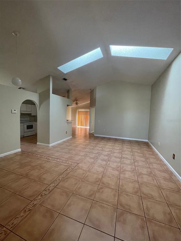 An open-concept living area features vaulted ceilings with skylights and tan tile flooring — 4312 IVEYGLEN AVENUE, ORLANDO, FL