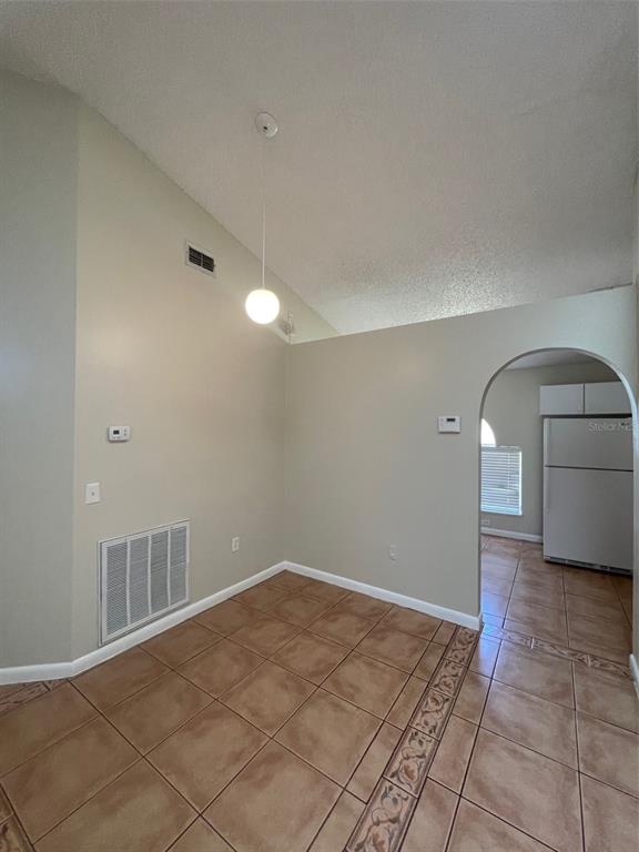 A dining area with tiled floors, a vaulted ceiling, and an arched entryway to the kitchen — 4312 IVEYGLEN AVENUE, ORLANDO, FL