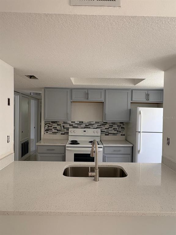 A kitchen with gray cabinets, white countertops, a stainless steel sink, and a white stove — 2803 FOX SQUIRREL, KISSIMMEE, FL