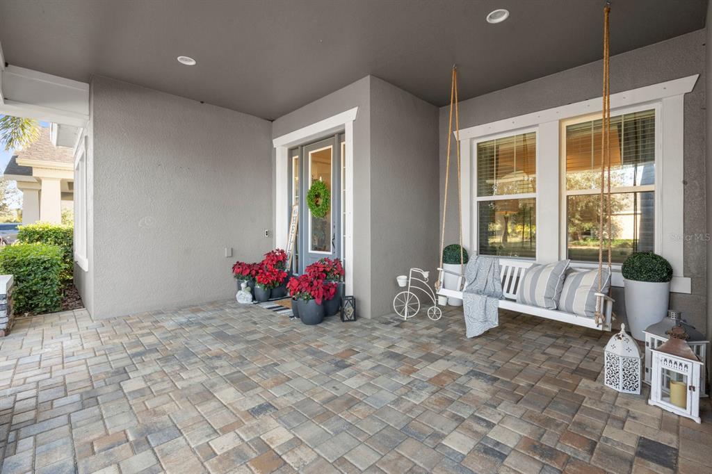 A covered front porch features a hanging bench, potted poinsettias, and decorative lanterns on pavers — 6440 TIDELINE DRIVE, APOLLO BEACH, FL
