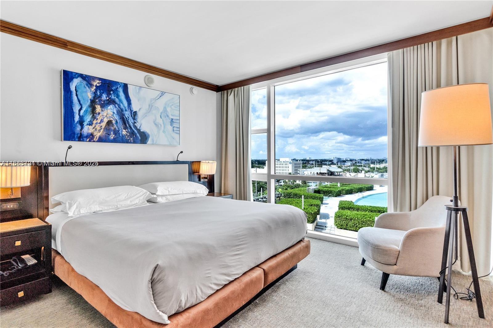 A bedroom features a king bed, a floor lamp, an armchair, and a large window — 6801 Collins Ave # 818, Miami Beach FL 33141, MIAMI BEACH, FL