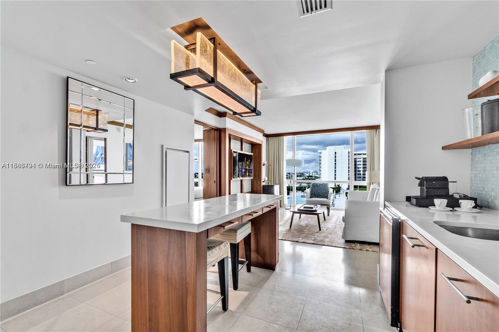 A modern kitchen with a wooden island and bar stools opens into a bright living area — 6801 Collins Ave # 818, Miami Beach FL 33141, MIAMI BEACH, FL