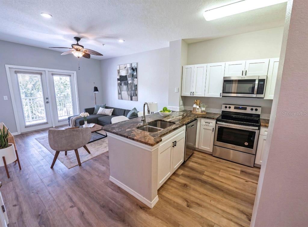 A kitchen with white cabinets and granite countertops overlooks a living area with wood flooring — 1810 E PALM AVENUE UNIT 1210, TAMPA, FL