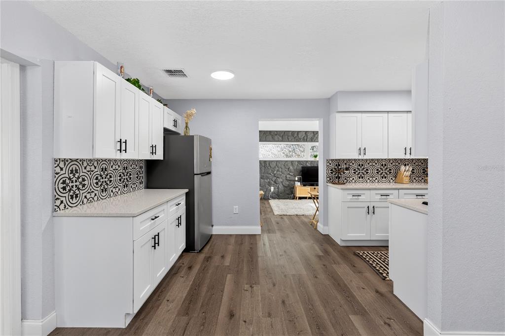 A kitchen features white cabinets, patterned tile backsplashes, stainless steel appliances, and wood-look flooring — 501 FITZGERALD DRIVE, MAITLAND, FL
