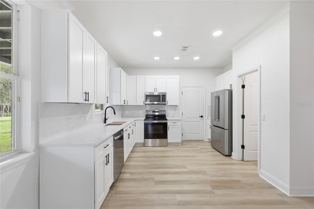 A modern kitchen features white cabinets, stainless steel appliances, light countertops, and wood-look flooring — 2124 CONTINENTAL STREET, ST CLOUD, FL