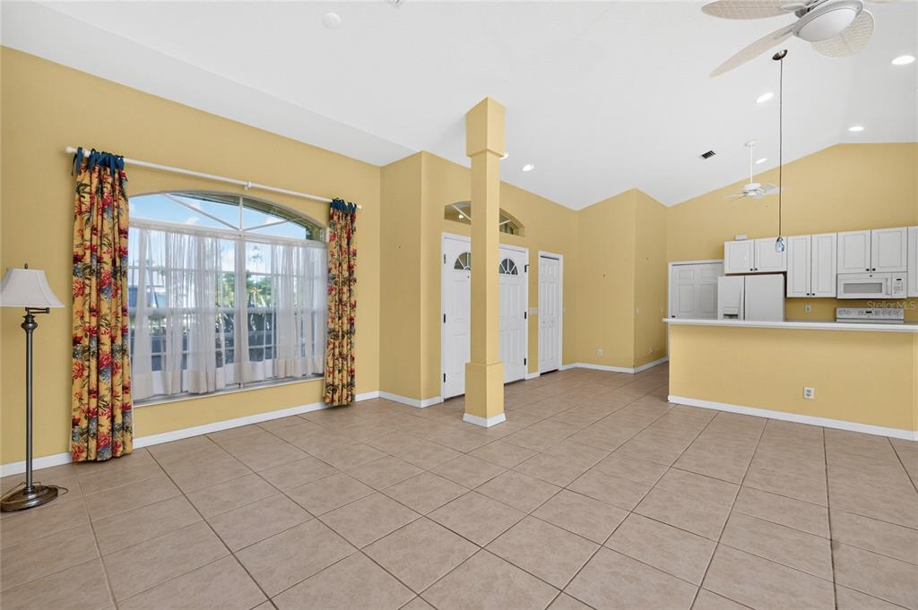 A living room with tile floors, yellow walls, a vaulted ceiling, and an open kitchen — 225 FAIRWAY ROAD, ROTONDA WEST, FL