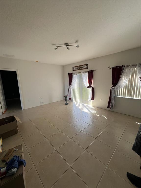An empty living room features beige tile flooring, a sliding glass door, and white walls — 735 COLVILLE PLACE, KISSIMMEE, FL