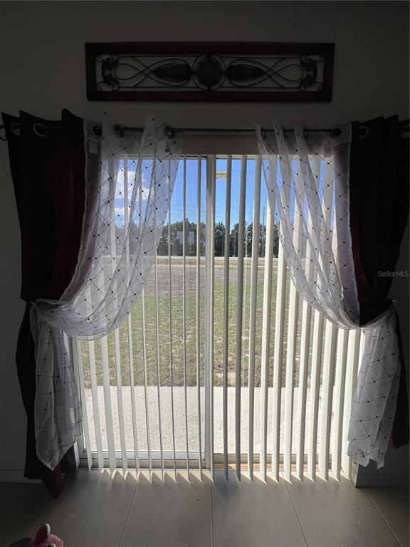 A sliding glass door with vertical blinds and layered curtains overlooks an outdoor grassy area — 735 COLVILLE PLACE, KISSIMMEE, FL