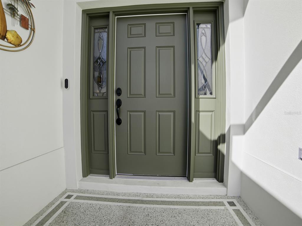 A sage green front door with sidelights and black hardware sits on a concrete porch — 3332 DALKEITH TERRACE, THE VILLAGES, FL