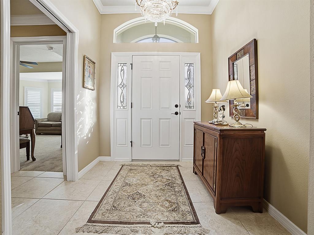 An entryway features a white front door, a crystal chandelier, tile flooring, and a wooden console — 3332 DALKEITH TERRACE, THE VILLAGES, FL