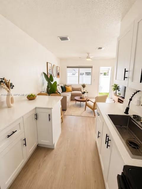 A modern kitchen with white cabinets and light wood flooring opens into a living area — 5712 Mayo St # 1, Hollywood FL 33023, HOLLYWOOD, FL