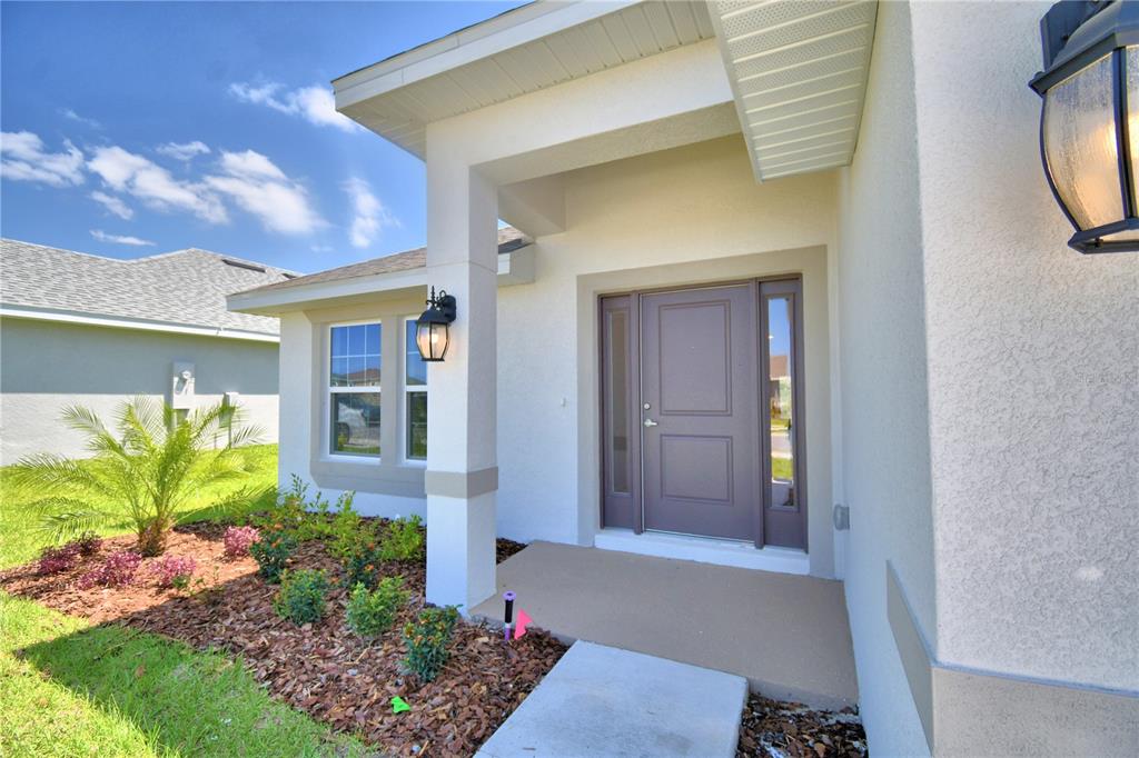 A beige stucco house exterior features a covered entryway with a brown front door — 4422 JUNEBERRY DRIVE, AUBURNDALE, FL
