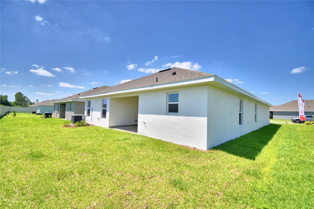 The exterior rear view of a white stucco house features a covered patio and lawn — 4422 JUNEBERRY DRIVE, AUBURNDALE, FL