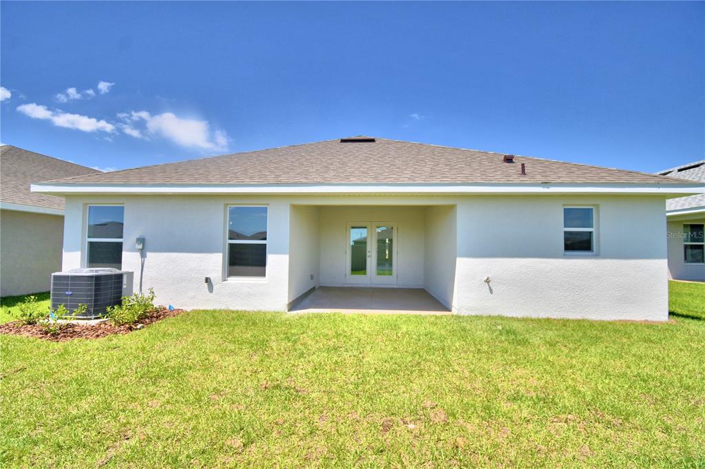 The rear exterior of a single-story house features a covered patio and a grassy yard — 4422 JUNEBERRY DRIVE, AUBURNDALE, FL
