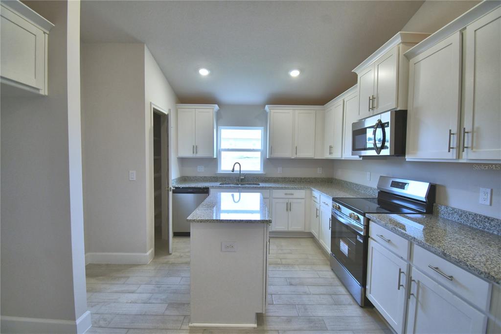 A kitchen features white cabinets, granite countertops, stainless steel appliances, and a central island — 4422 JUNEBERRY DRIVE, AUBURNDALE, FL