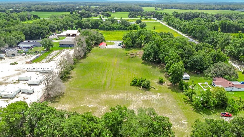 An aerial view shows a large, grassy lot bordered by trees, buildings, and parked trailers — 5298 CR 542F, BUSHNELL, FL