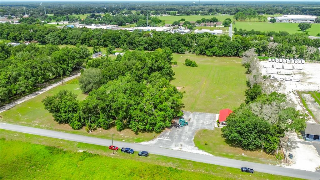 An aerial view shows a large grassy lot with trees, a paved parking area, and a building — 5298 CR 542F, BUSHNELL, FL
