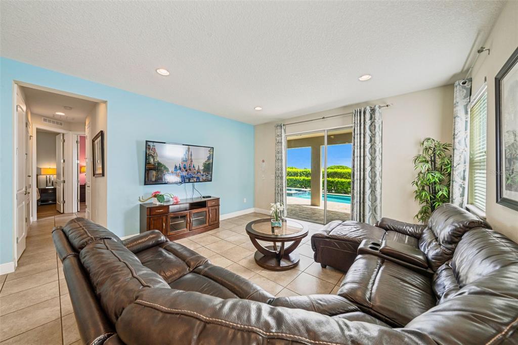 A living room features a blue accent wall, leather sectional, and sliding doors to a pool — 231 LASSO DRIVE, KISSIMMEE, FL
