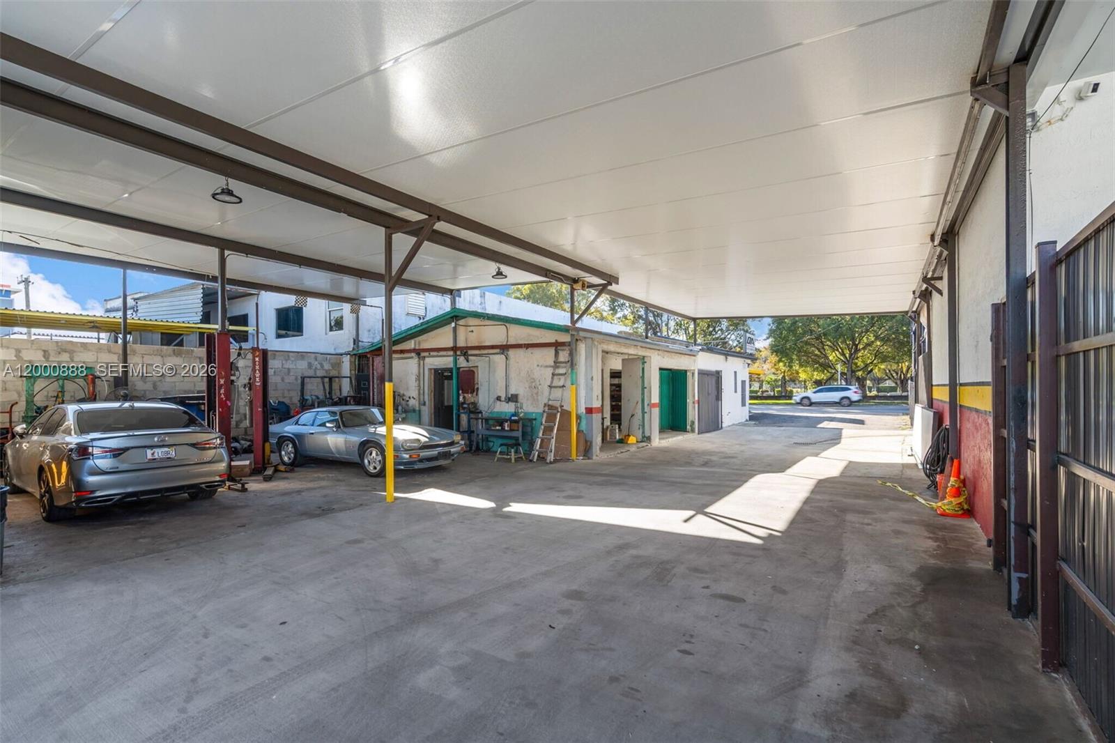 An outdoor covered work area with concrete flooring, a car lift, and two parked cars — 3219 SW 8th St, Miami FL 33135, MIAMI, FL