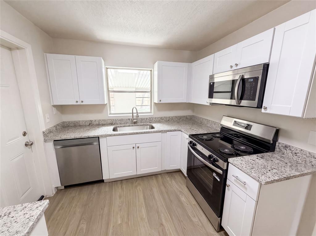 A kitchen features white cabinets, granite countertops, stainless steel appliances, and light wood-look flooring — 585 HEWETT DRIVE, ORLANDO, FL
