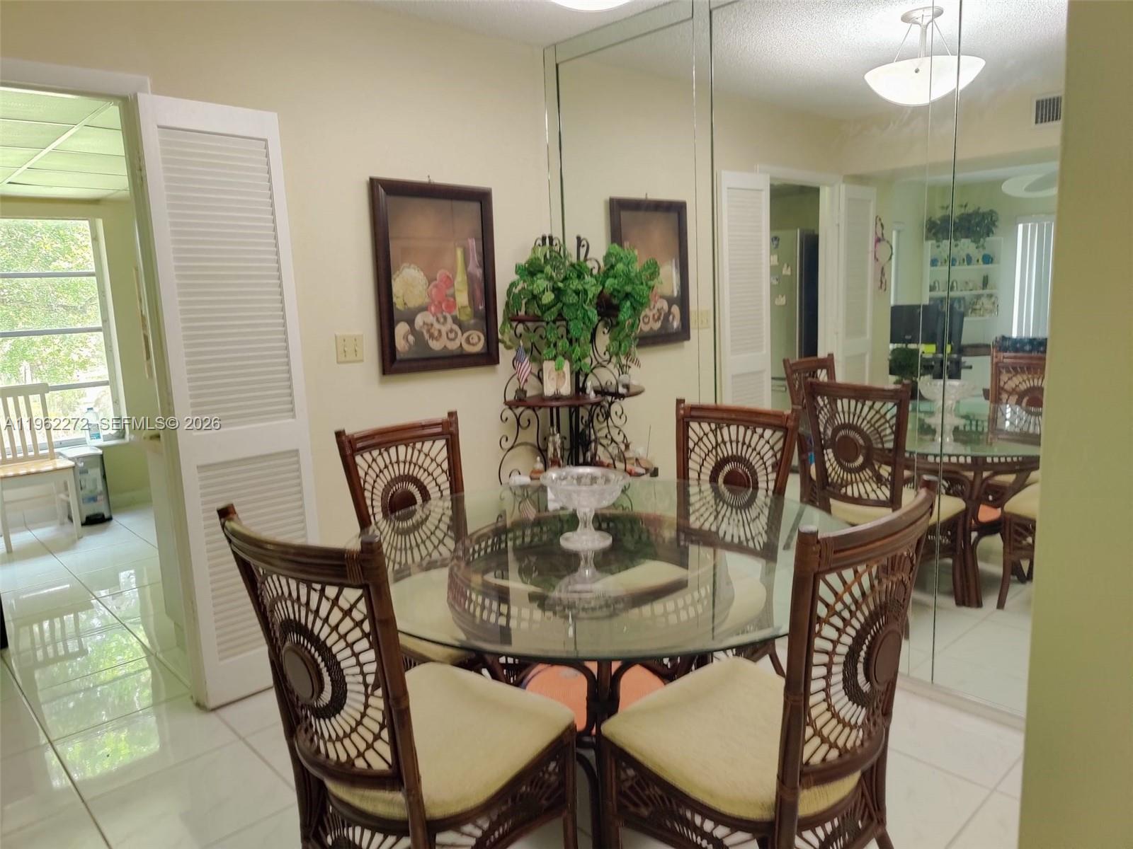 A dining room features a glass-topped table, rattan chairs, and a large mirrored wall — 4168 Inverrary Dr # 301, Lauderhill FL 33319, LAUDERHILL, FL