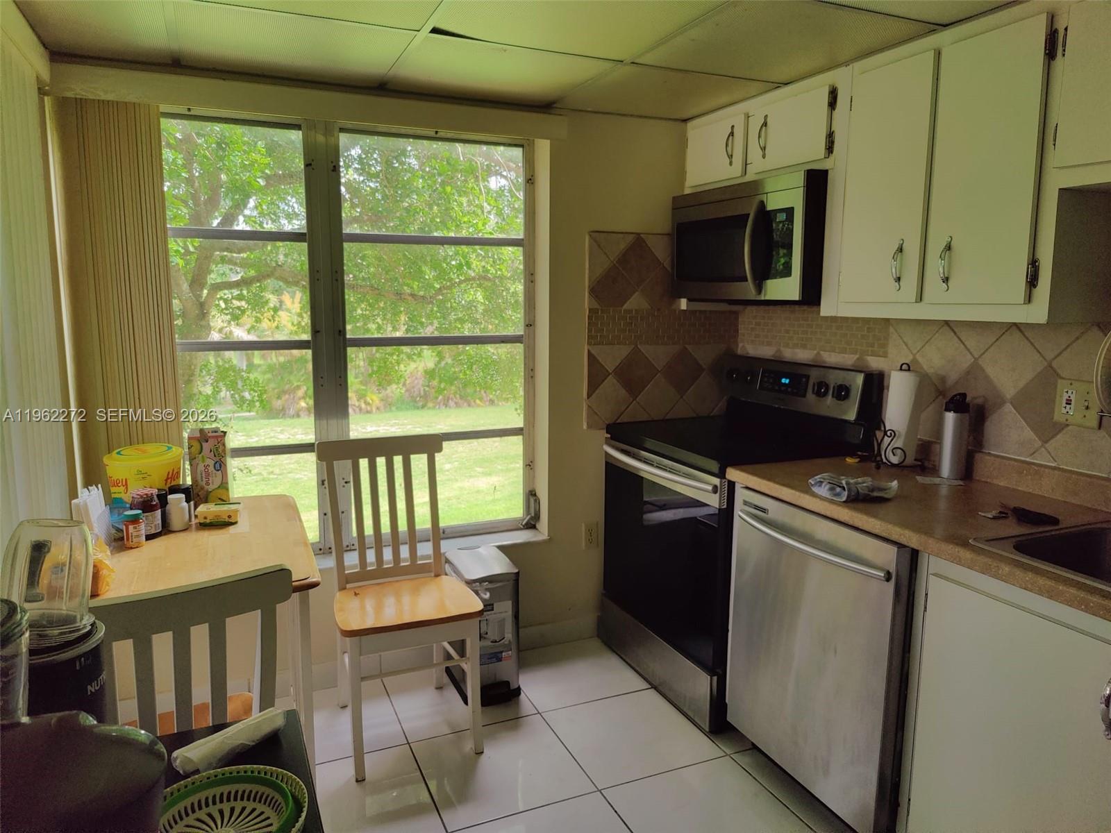 A kitchen features white cabinets, stainless steel appliances, tile flooring, and a windowed dining area — 4168 Inverrary Dr # 301, Lauderhill FL 33319, LAUDERHILL, FL