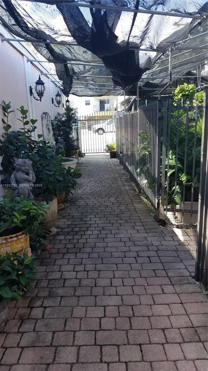 A paved walkway leads to a metal gate, flanked by potted plants and wall sconces — 1239 Alton Rd # 2, Miami Beach FL 33139, MIAMI BEACH, FL