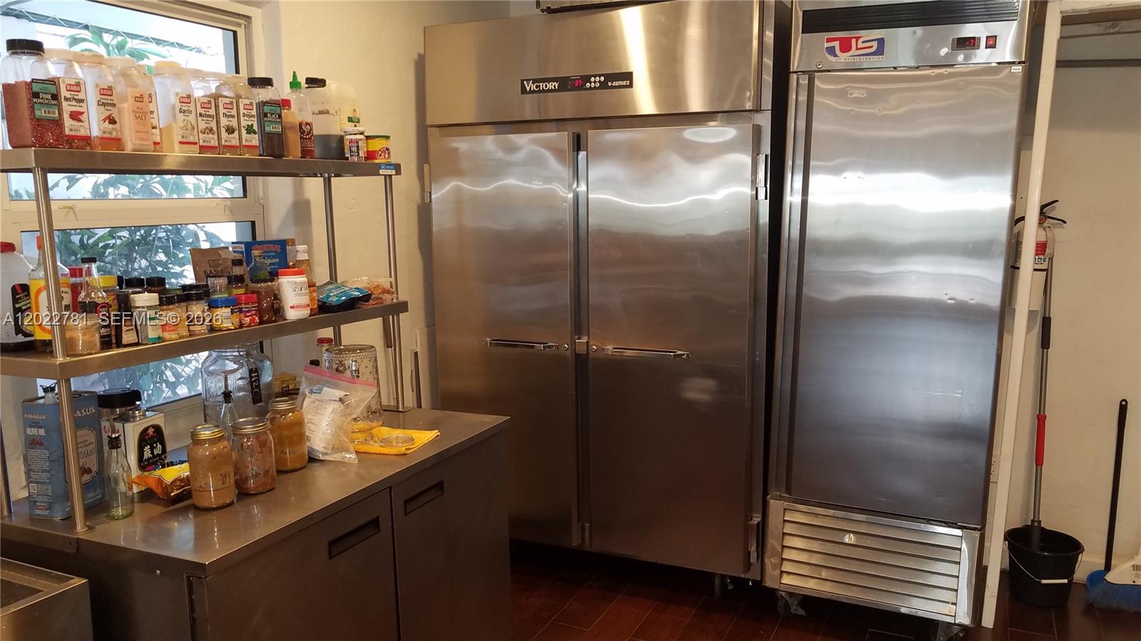 A commercial kitchen features stainless steel refrigerators, metal shelving, and various spice containers — 1239 Alton Rd # 2, Miami Beach FL 33139, MIAMI BEACH, FL