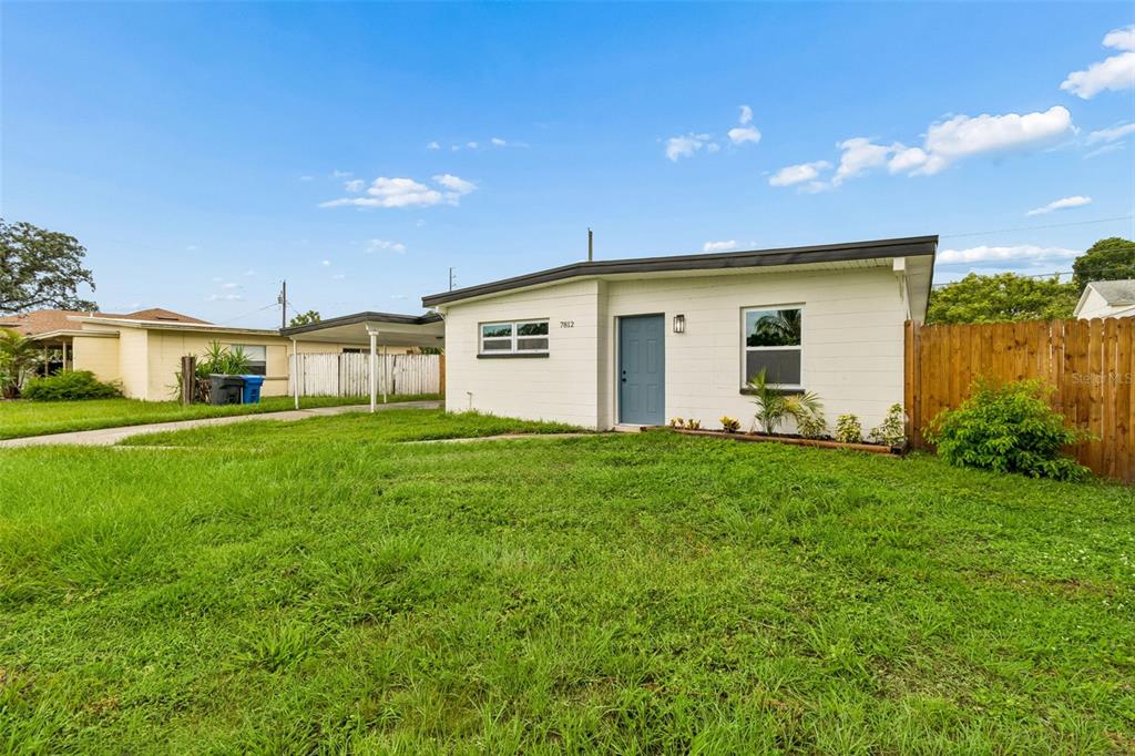 A white single-story house with a blue front door and a wooden fence — 7812 EGYPT LAKE DRIVE, TAMPA, FL