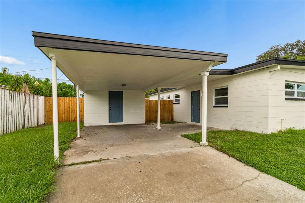 A white house exterior features a concrete carport with two blue doors and a fence — 7812 EGYPT LAKE DRIVE, TAMPA, FL