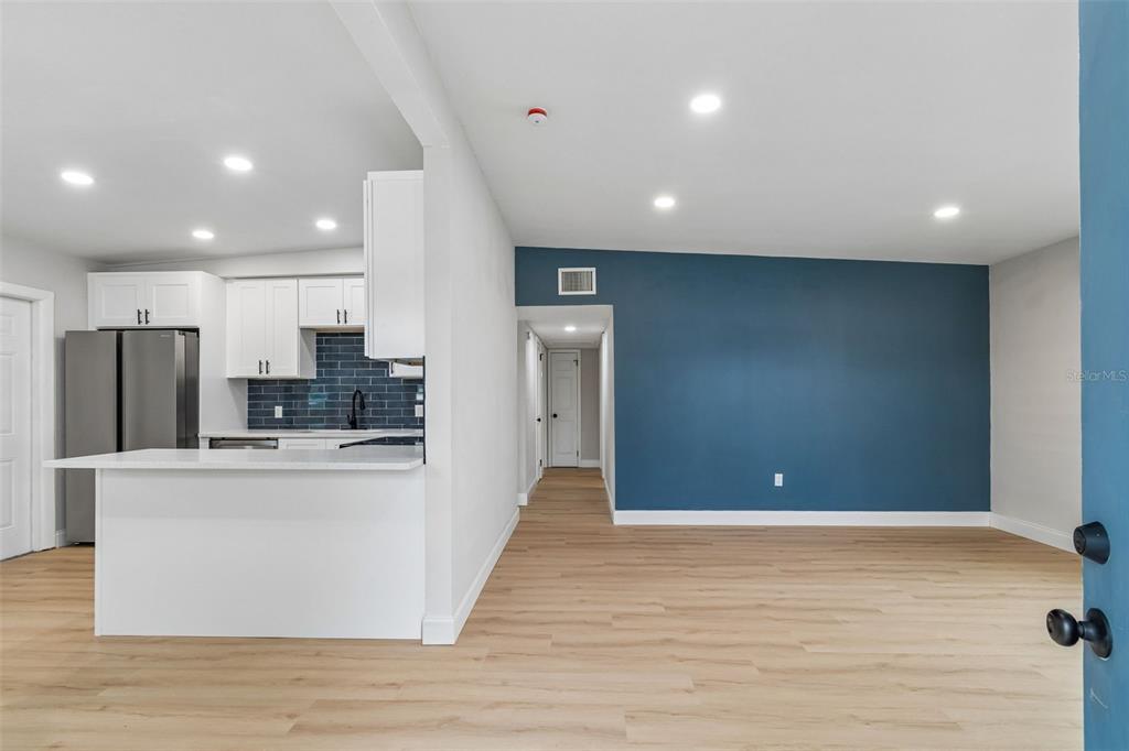 A kitchen with white cabinets and a blue backsplash opens into a living area — 7812 EGYPT LAKE DRIVE, TAMPA, FL