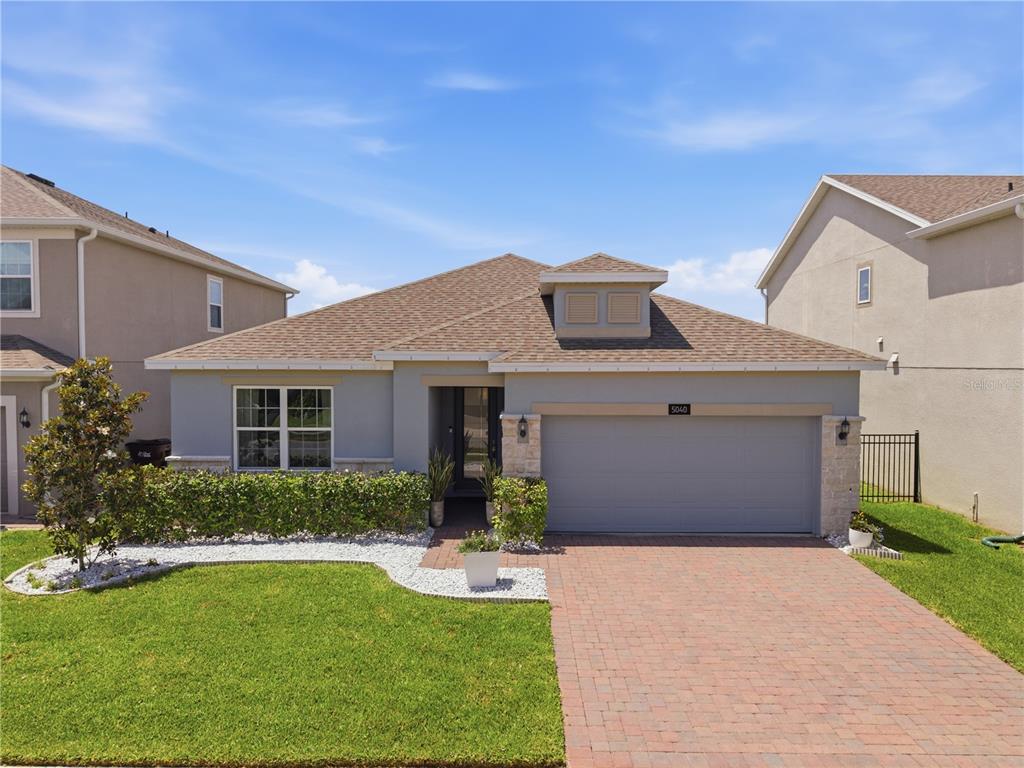 A single-story house with a gray exterior, stone accents, a two-car garage, and a driveway — 5040 BESSIE COURT, ST CLOUD, FL