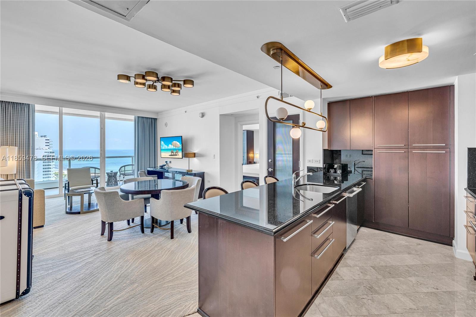 A modern kitchen with dark cabinetry and granite countertops opens into a dining and living area — 4391 Collins Ave, Miami Beach FL 33140, MIAMI BEACH, FL