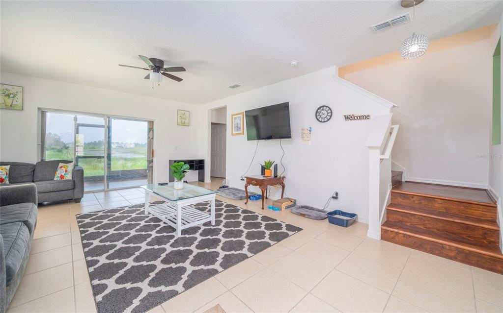 A living room features tile flooring, a patterned area rug, a television, and wooden stairs — 212 PRIMROSE DRIVE, DAVENPORT, FL