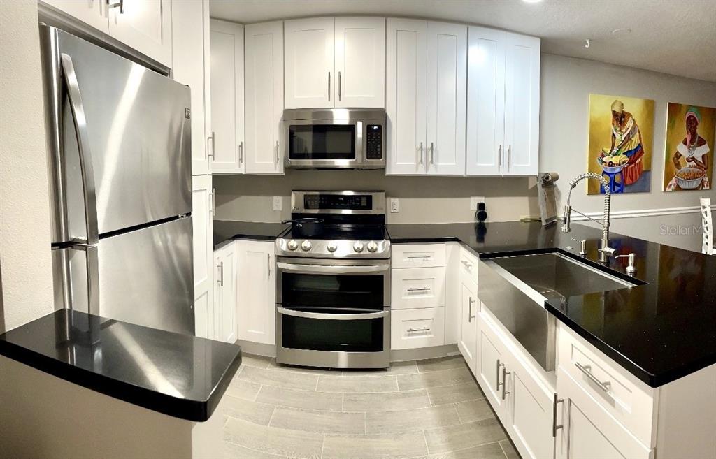 A kitchen features white cabinets, stainless steel appliances, black countertops, and a farmhouse sink — 5171 LAZY OAKS DRIVE, WINTER PARK, FL