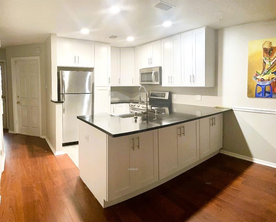 A kitchen features white cabinets, stainless steel appliances, a dark countertop island, and wood flooring — 5171 LAZY OAKS DRIVE, WINTER PARK, FL