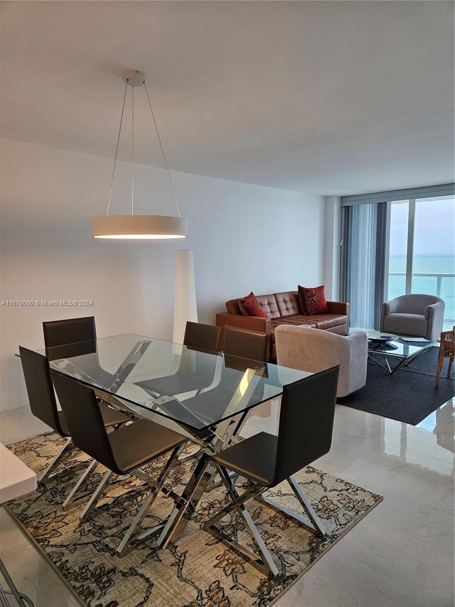 A modern dining and living area features a glass table, leather sofa, and ocean views — 5601 Collins Ave # 1605, Miami Beach FL 33140, MIAMI BEACH, FL