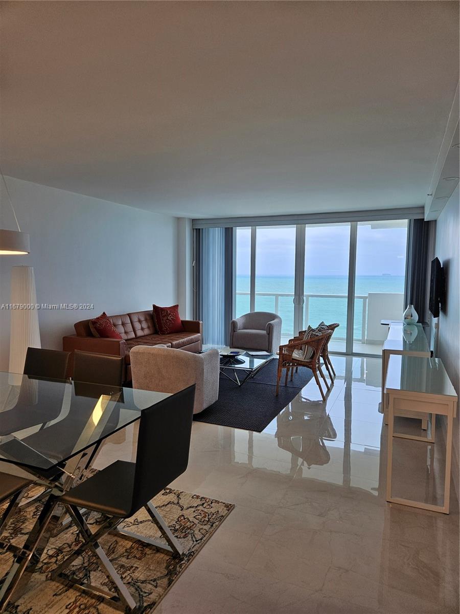 A living and dining area features tile floors, modern furniture, and a balcony overlooking the ocean — 5601 Collins Ave # 1605, Miami Beach FL 33140, MIAMI BEACH, FL
