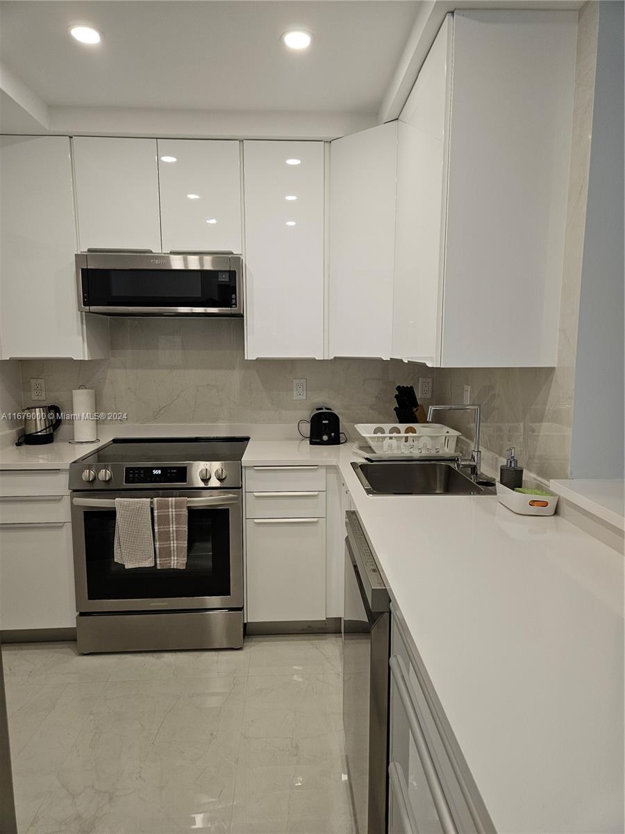 A modern kitchen features white cabinets, stainless steel appliances, and light-colored stone countertops — 5601 Collins Ave # 1605, Miami Beach FL 33140, MIAMI BEACH, FL