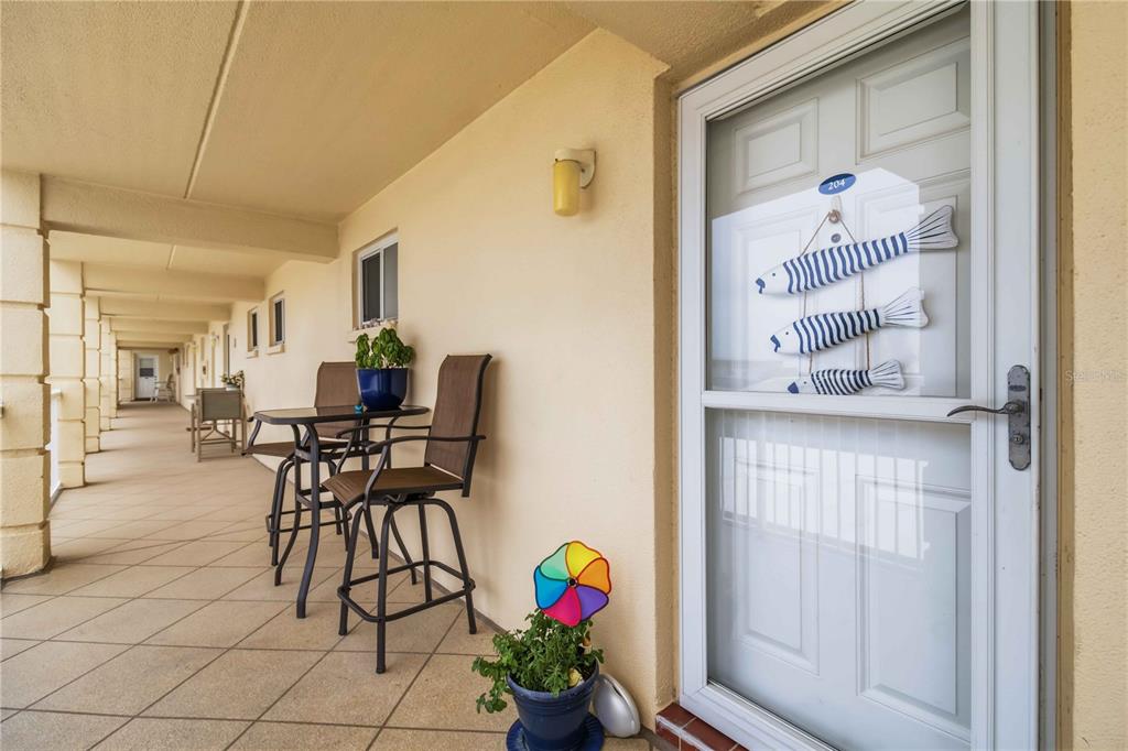 A covered outdoor balcony features a small table, two chairs, and a decorative fish ornament — 3804 GULF OF MEXICO DRIVE UNIT B204, LONGBOAT KEY, FL