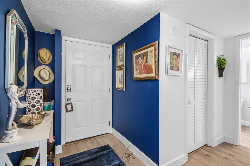 An entryway features a white door, blue accent walls, wood-look flooring, and decorative wall art — 3804 GULF OF MEXICO DRIVE UNIT B204, LONGBOAT KEY, FL