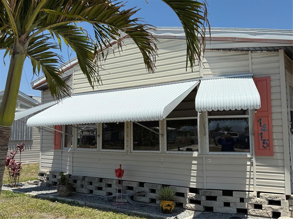 The exterior of a mobile home features light siding, metal awnings, and a concrete block foundation — 1415 BLUE HERON DRIVE, ENGLEWOOD, FL