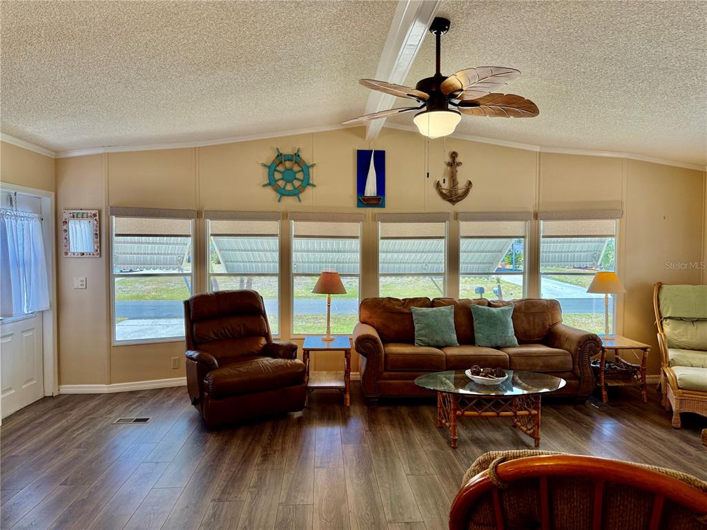 A living room features wood-look flooring, a brown sofa, a recliner, and nautical wall decor — 1415 BLUE HERON DRIVE, ENGLEWOOD, FL