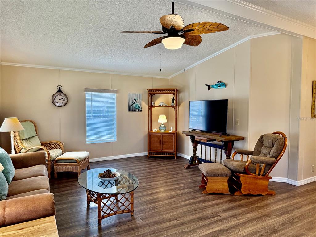 A living room features wood-look flooring, a ceiling fan, a television, and wicker furniture — 1415 BLUE HERON DRIVE, ENGLEWOOD, FL