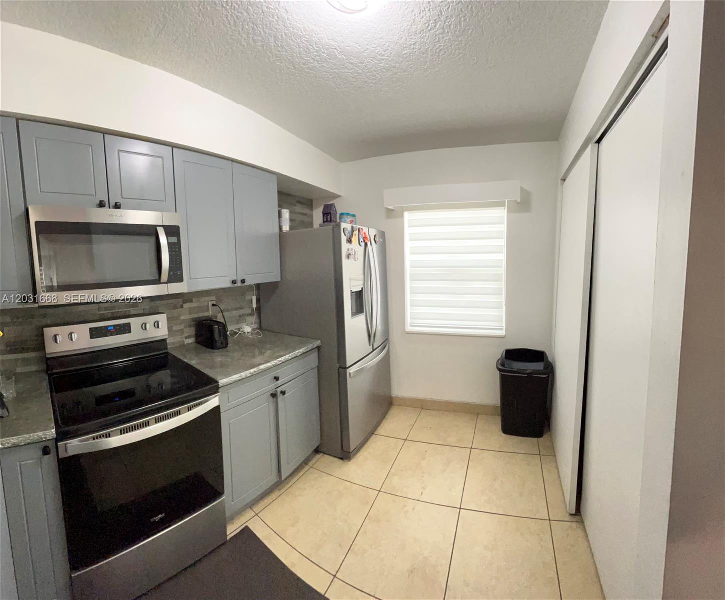 A kitchen features gray cabinets, stainless steel appliances, a tiled floor, and a window — 9206 SW 147th Ct, Miami FL 33196, MIAMI, FL