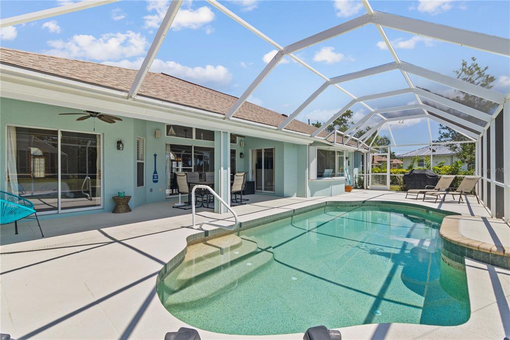 A swimming pool with a screened-in lanai and patio area behind a light blue house — 54 MEDALIST PLACE, ROTONDA WEST, FL