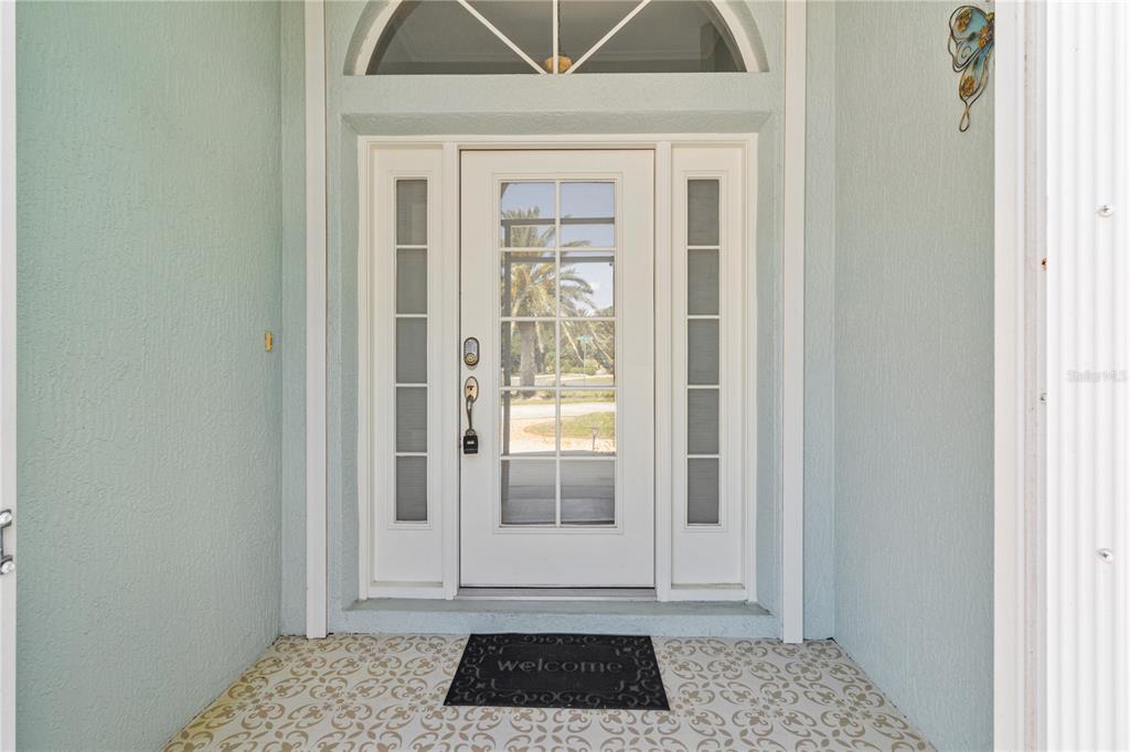 A white front door with glass panels and sidelights is framed by light blue walls — 54 MEDALIST PLACE, ROTONDA WEST, FL