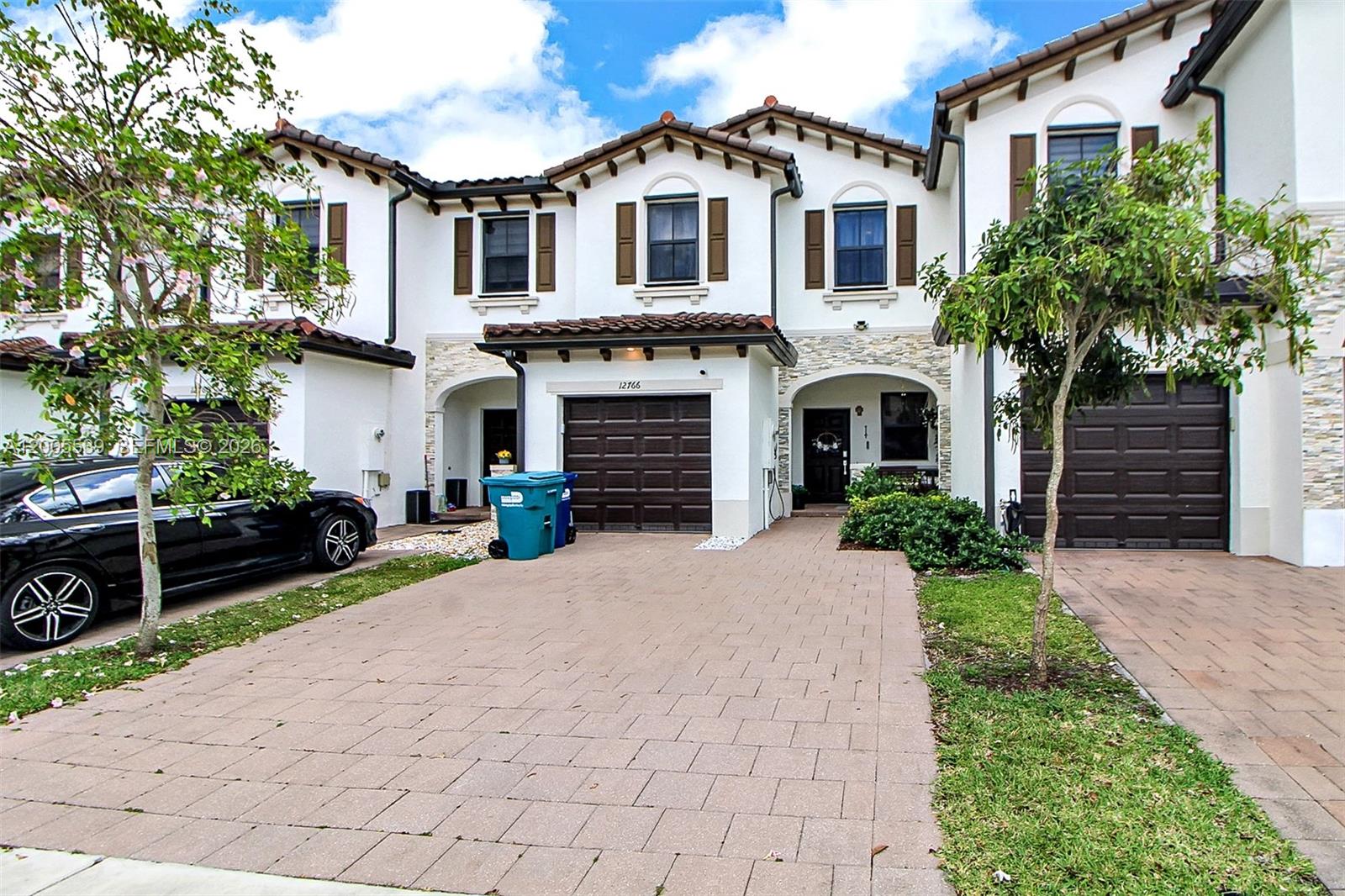A multi-story townhouse exterior features white stucco walls, brown garage doors, and a paved driveway — 12766 SW 229th Ter, Miami FL 33170, MIAMI, FL