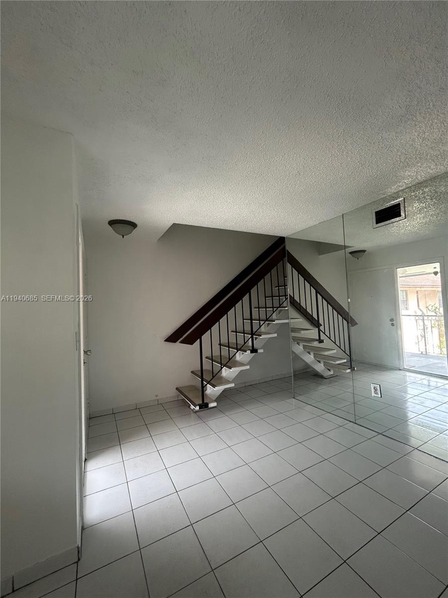 A room with white tile floors, a staircase with dark railings, and a mirrored wall — 5851 W 20th Ave # 409, Hialeah FL 33012, HIALEAH, FL