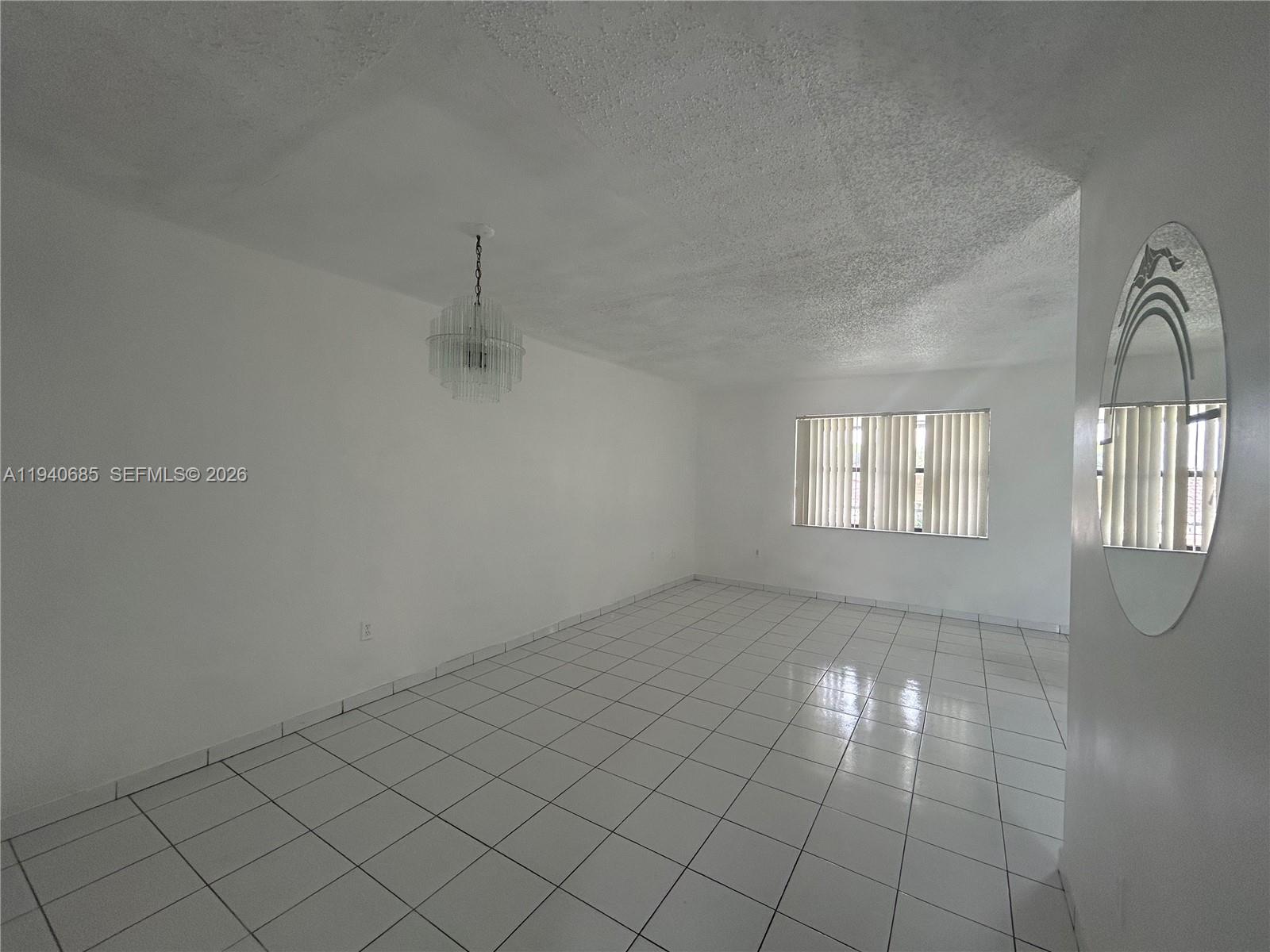 A dining room features white tiled floors, a crystal chandelier, and a large oval mirror — 5851 W 20th Ave # 409, Hialeah FL 33012, HIALEAH, FL